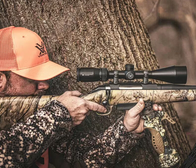 Camouflage-Gewehr mit Zielfernrohr im Einsatz Person in Tarnkleidung zielt mit einem Gewehr mit Zielfernrohr im Wald.