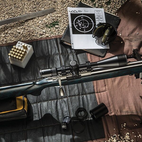 Präzisionsschützen-Ausrüstung mit Zielfernrohr und Munition Präzisionsgewehr mit Zielfernrohr, Munition, Schießscheibe und Zubehör auf einer Matte beim Schießstand