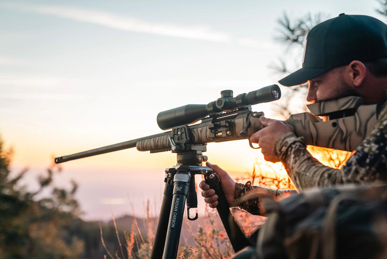 Eine Person zielt mit einem Gewehr auf einem Stativ im Sonnenuntergang